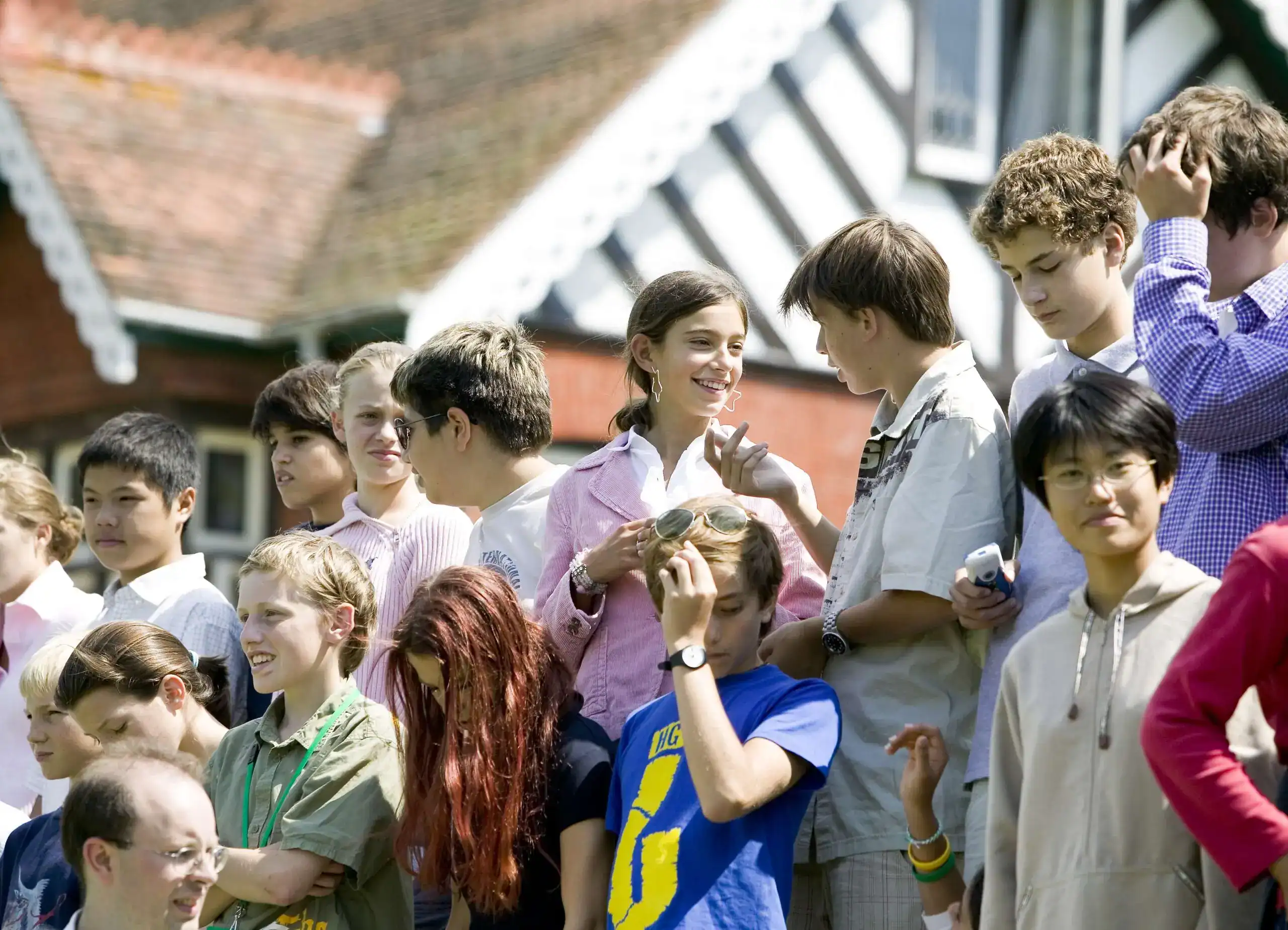 Diverse group of students outdoors at a school event in England, sunny day, engaging in lively conversations.