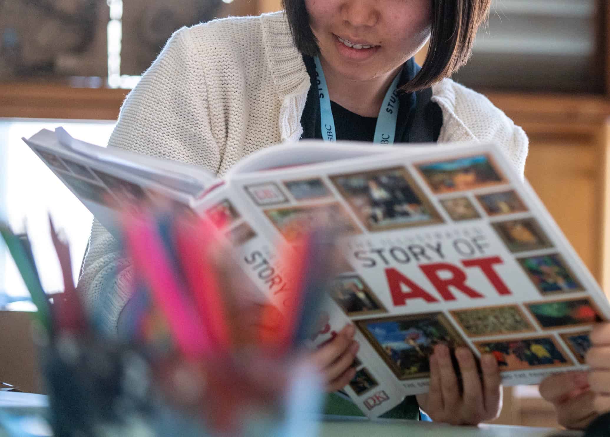 Bright girl reading a colourful art history book in classroom setting.