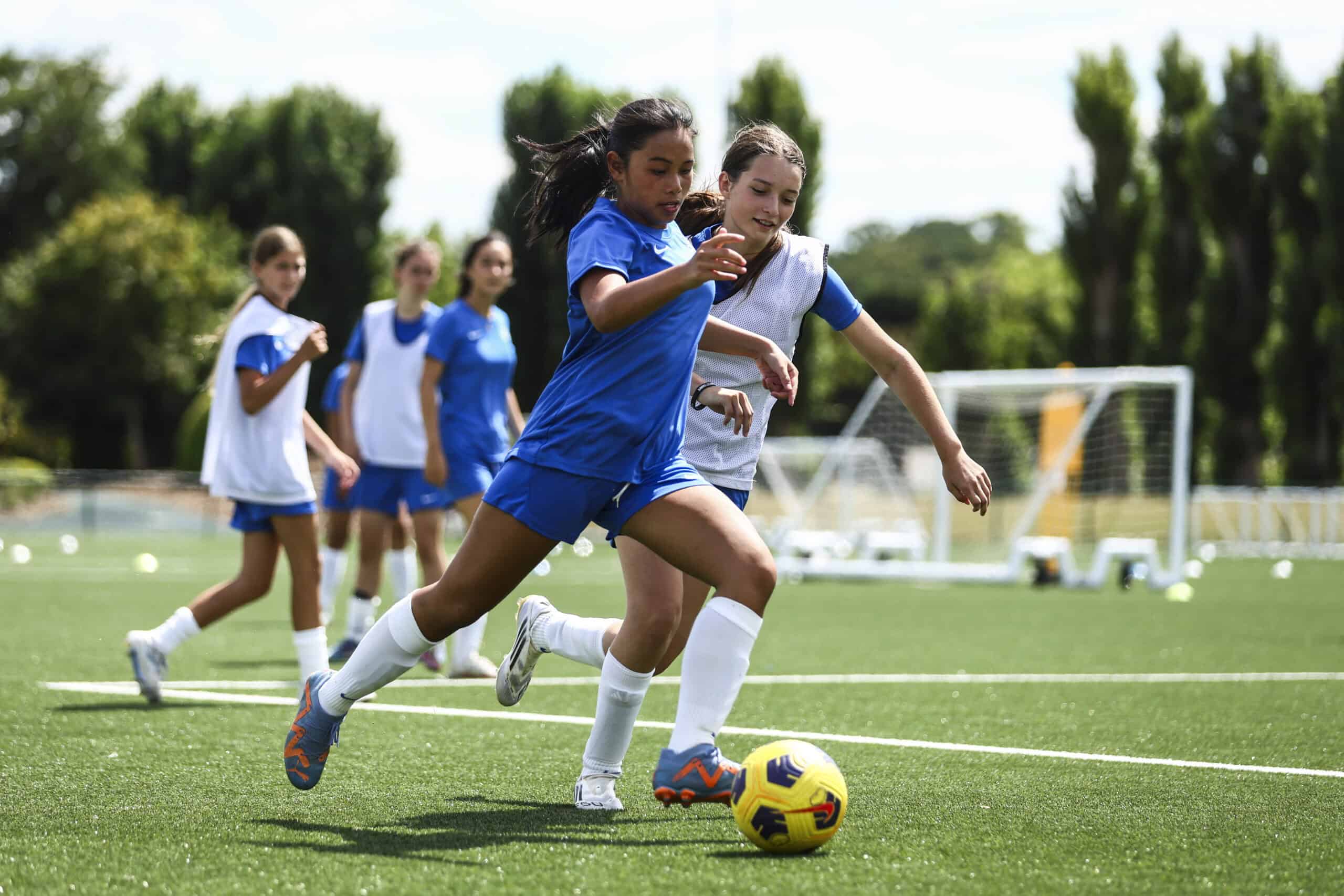 Girls playing soccer on a field, sports activity at school, summer sports programme.